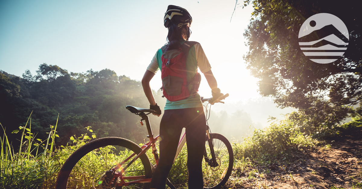 Woman with a bike looking at sun shining