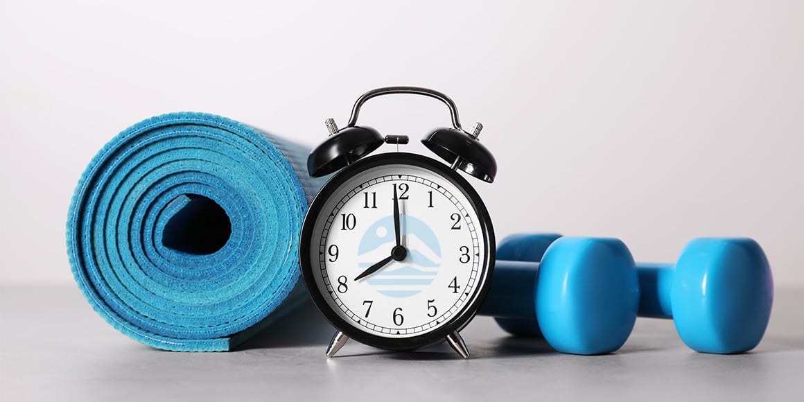 Blue yoga mat sitting next to a black wind-up alarm clock and two small blue hand weights.