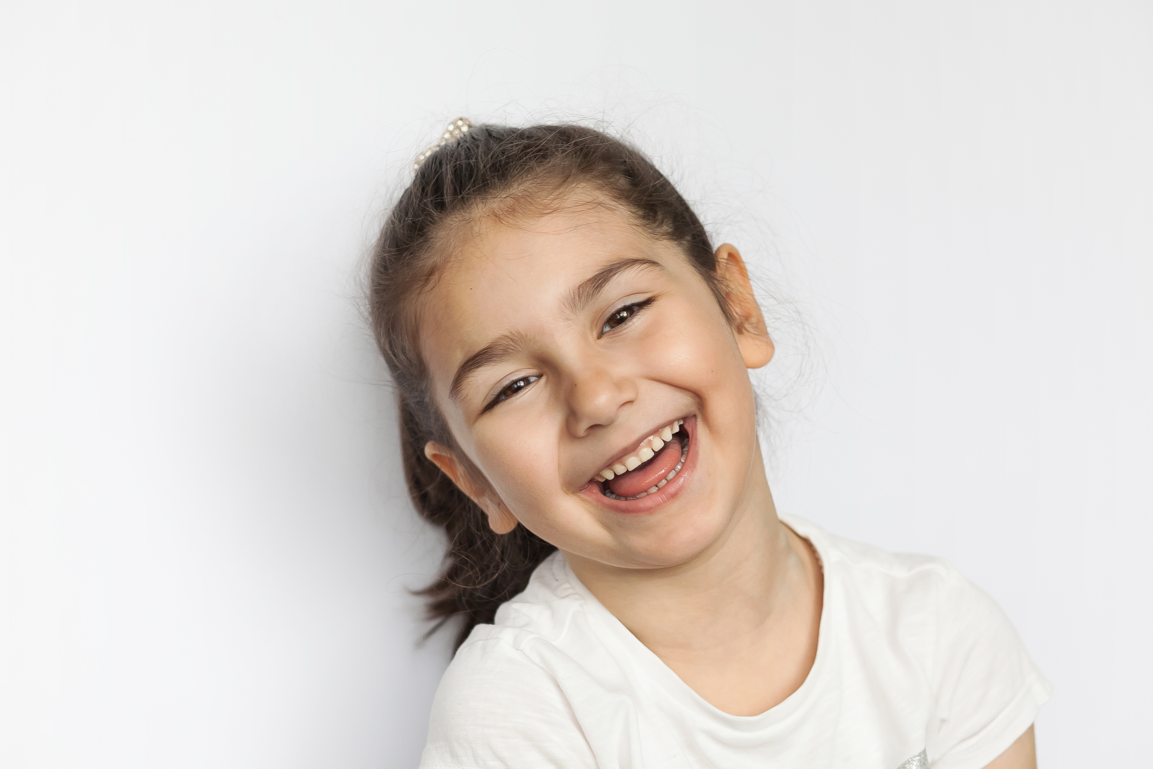 child with brown hair laughing grey background