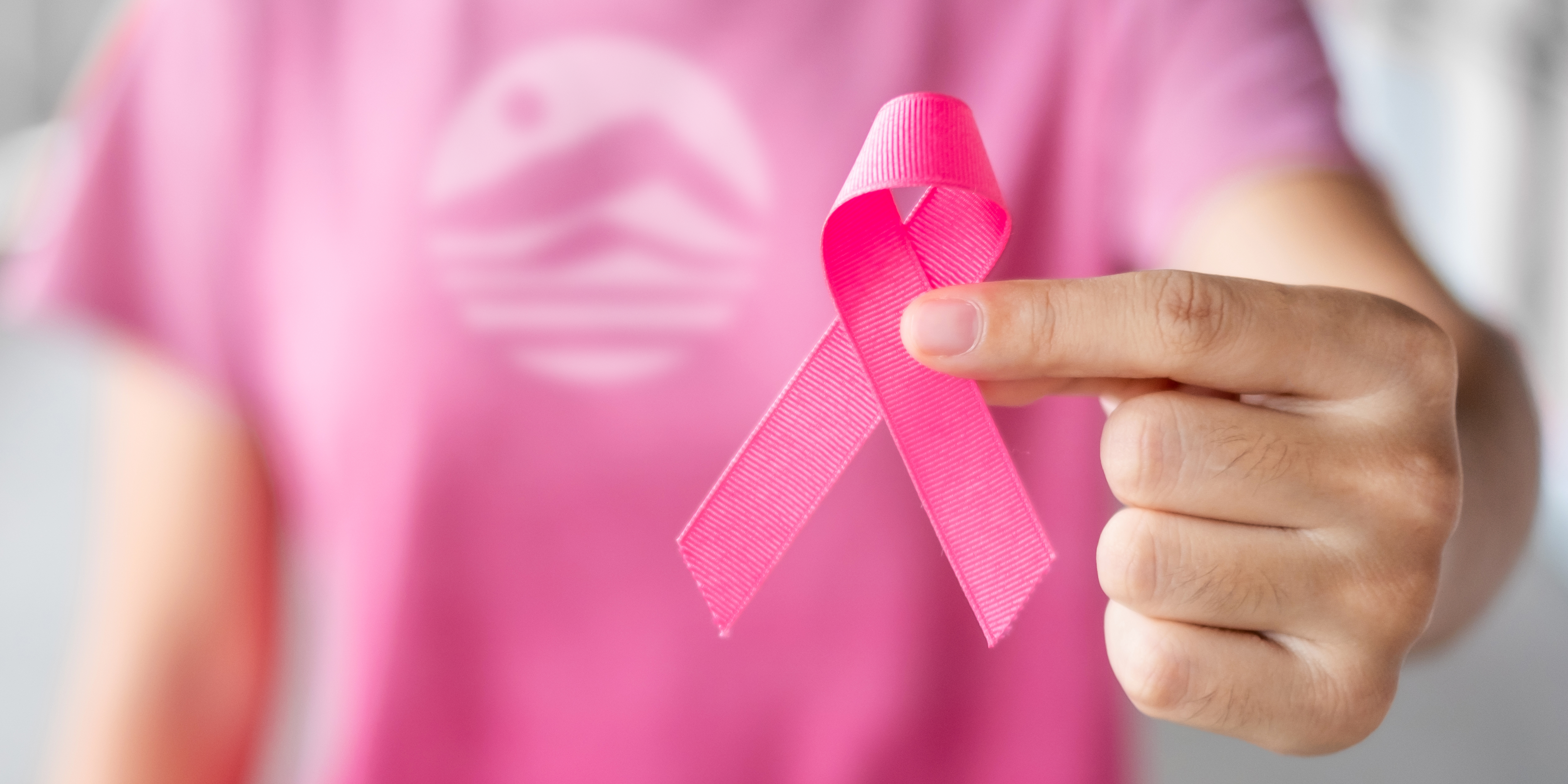 A woman in a pink Alaska Club shirt holds a pink ribbon out, representing breast cancer awareness.