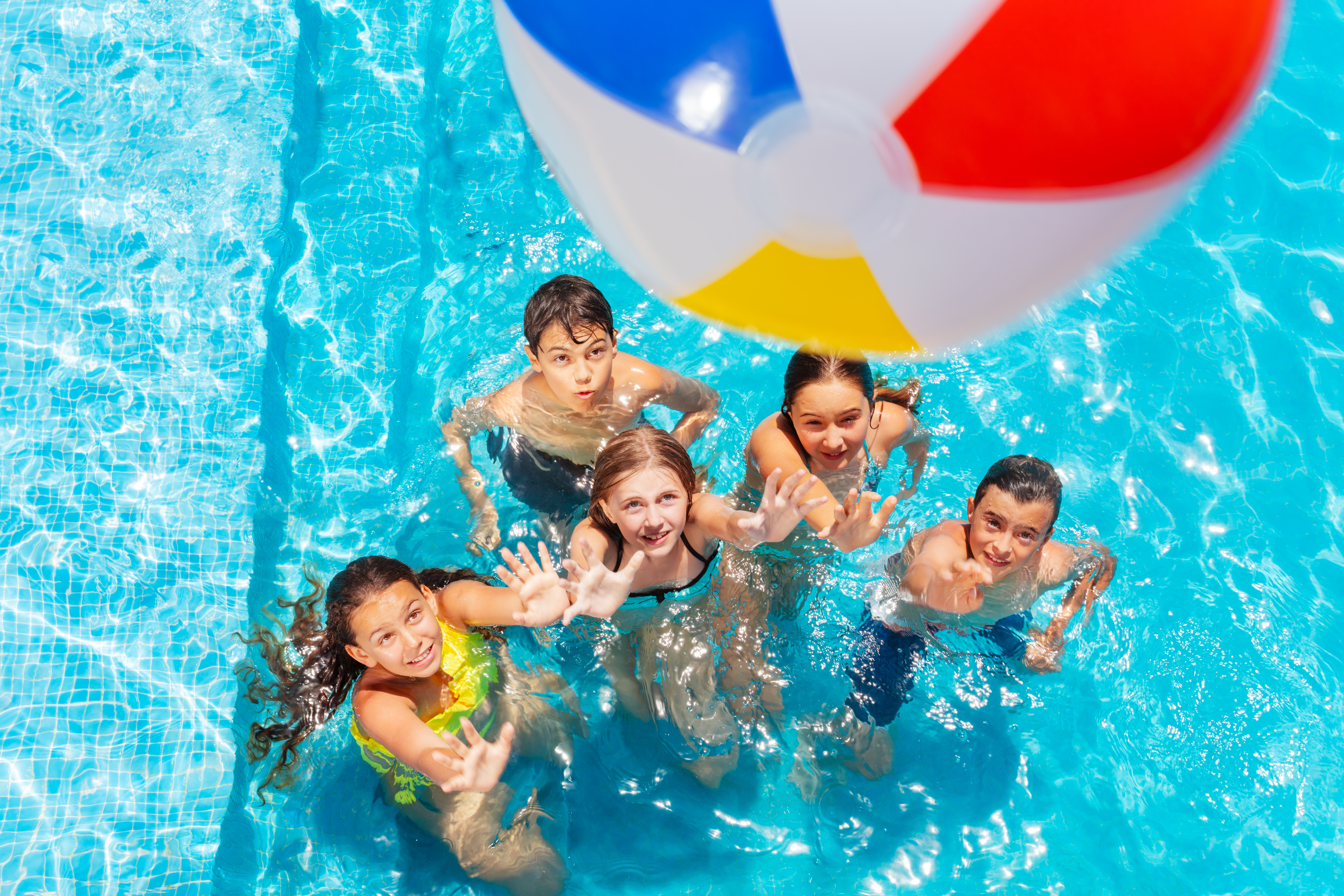 five children in pool playing with beach ball